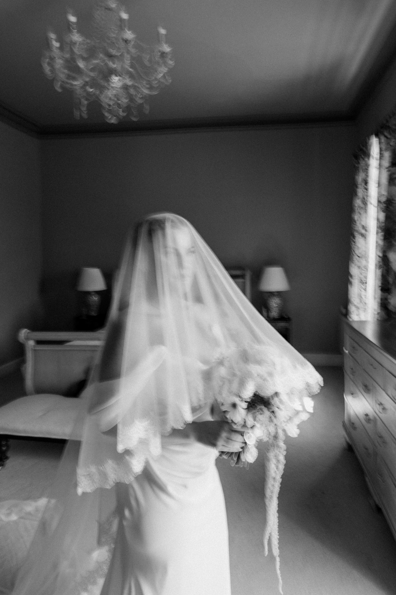 Bride in a tiered tulle veil holding a trailing bouquet, in black and white